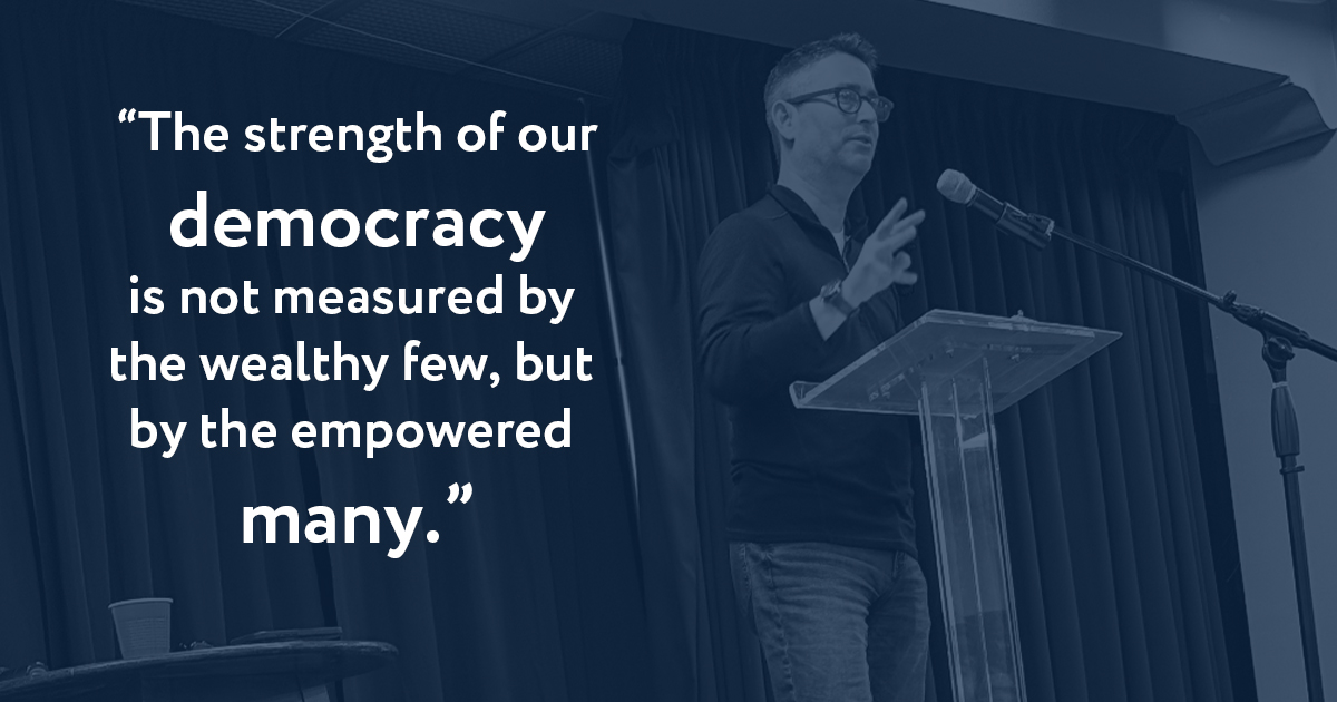 Steve Smith speaking at a podium with the words, "The strength of our democracy is not measured by the wealthy few, but by the empowered many."